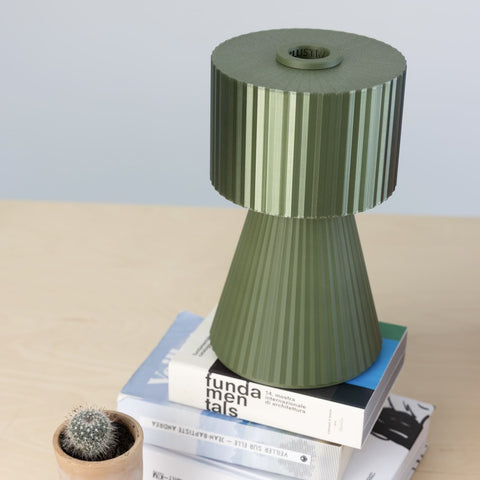 Lustra Plissé table lamp in Forest Green placed on books in a cozy interior