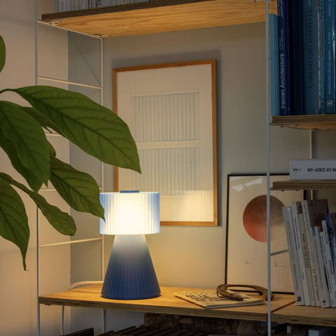Lustra Plissé table lamp in Ocean Blue styled on shelf with framed art and plant