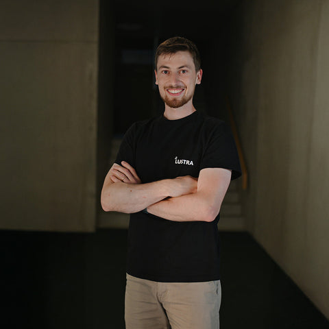 Man wearing a black t-shirt with a logo, standing against a dark background